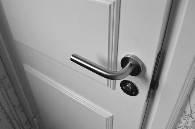 Detail na biele zatvorené dvere so striebornou kľučkou 