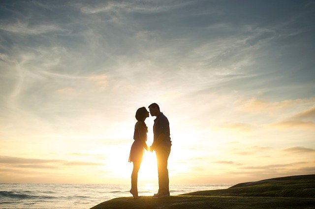 Žena a muž sa bozkávajú pri západe slnka 